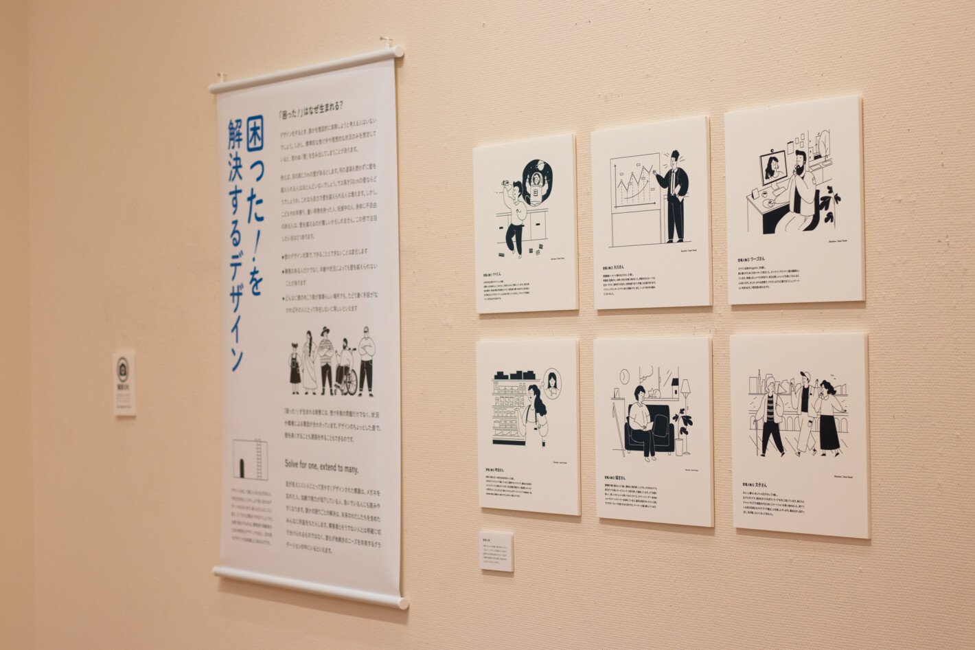 写真:「困った!を解決するデザイン」というタペストリーと、6人の登場人物のイラストとプロフィールが書かれたパネルの展示。