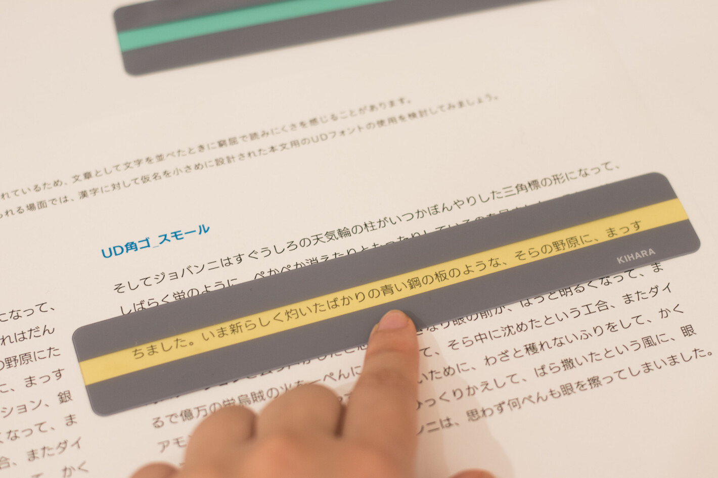 写真:UD角ゴ スモールで書かれた文章の上にイエローのリーディングトラッカーをあてています。リーディングトラッカーは定規のような形で、読んでいる1行をハイライトし、前後の行を隠す道具です。