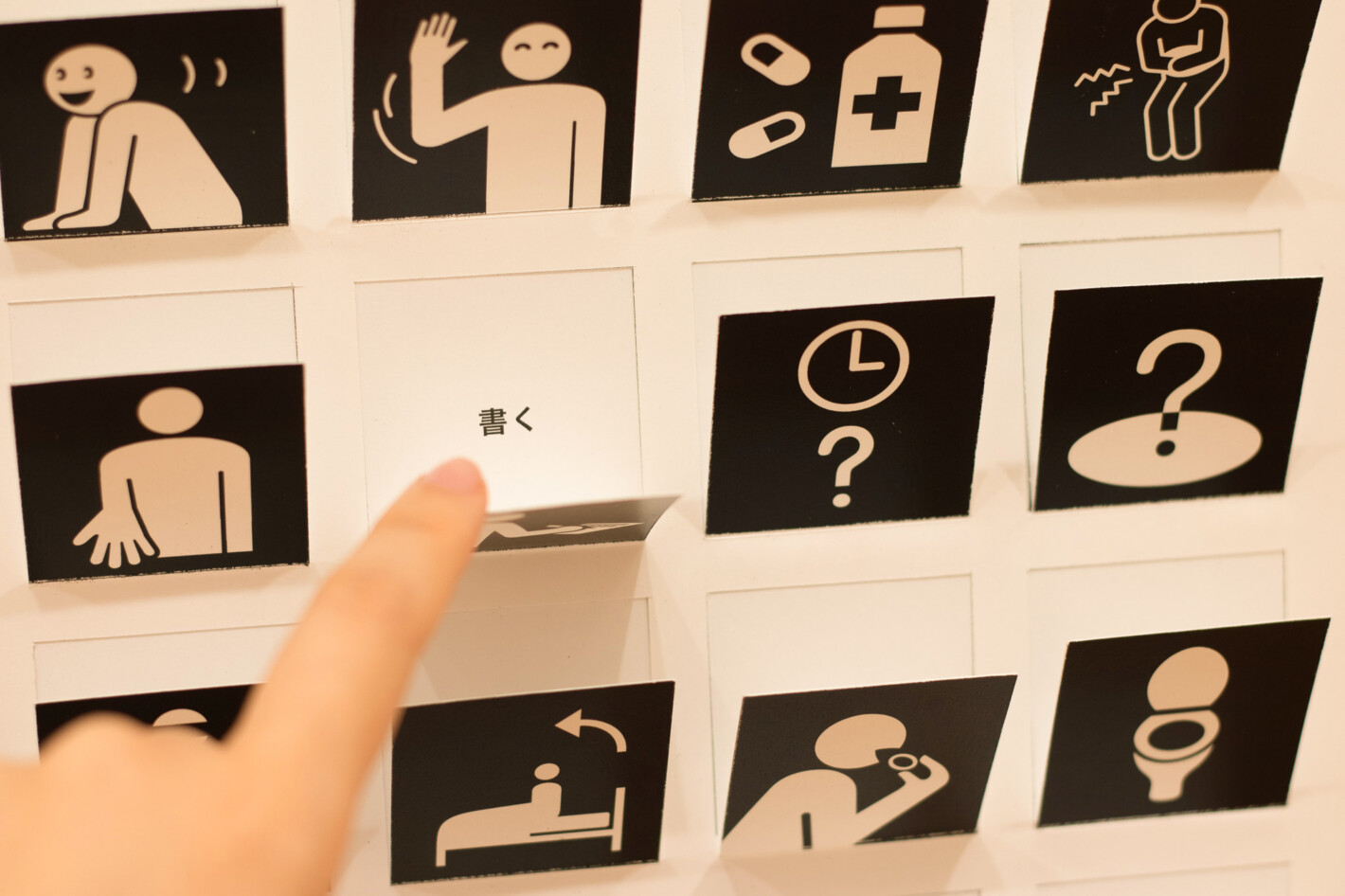写真:正方形の絵記号が並んだパネルに切り込みが入っています。1つの絵記号をめくって「書く」という文字が見えているところ。