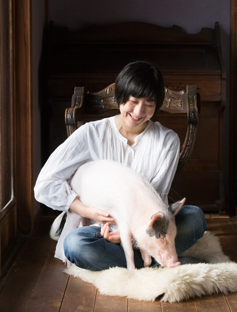 わたしとうたちゃんのポートレイト写真。縁側に座って、小脇に子豚を抱えて笑っています。
