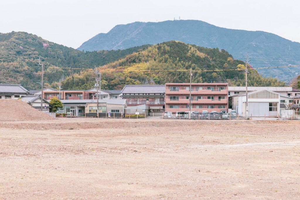 写真:まだ何も建っていない広い更地。向こうには住宅や山が見えます。