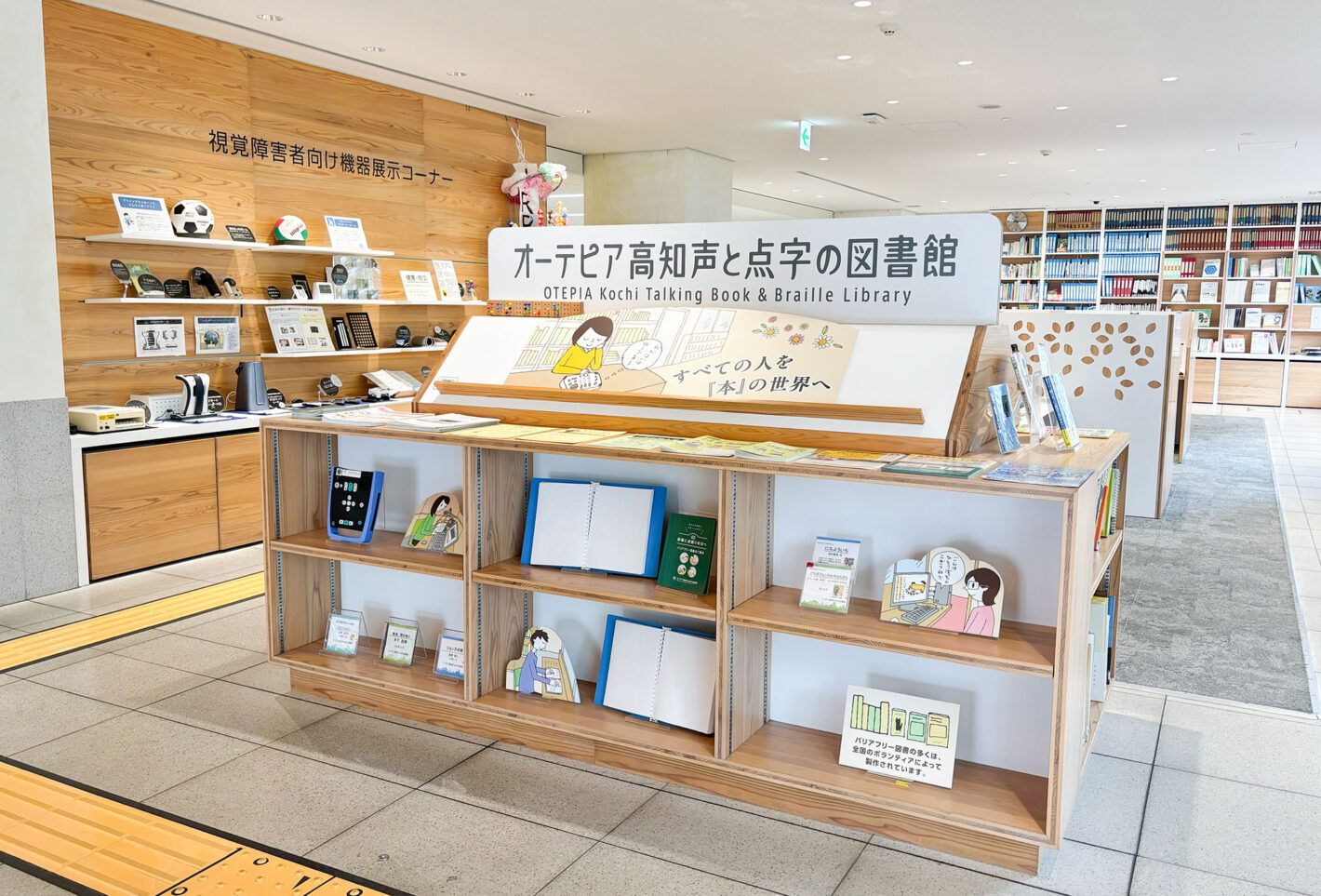 写真:オーテピア声と点字の図書館の入り口。「すべての人を本の世界へ」と書かれた棚に点字資料や録音図書が置いてあります。壁際には視覚障害者向け機器展示コーナーがあります。