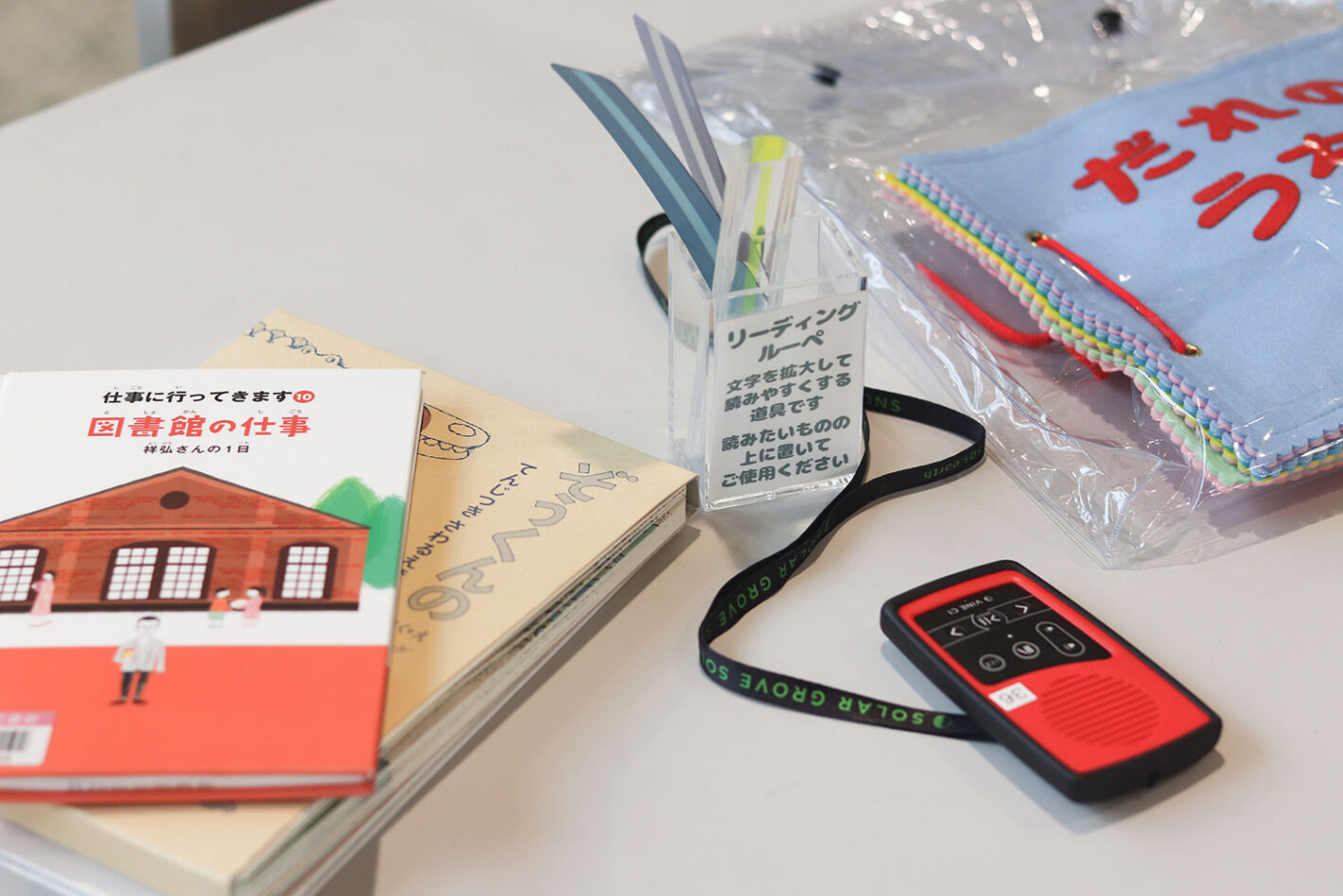 写真:机の上に置いた本、リーディングルーペ、赤い録音再生機